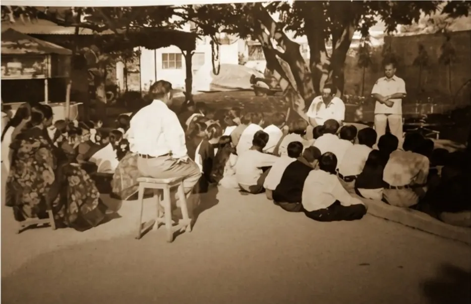Sepia photograph of children seated under trees with their teachers.
